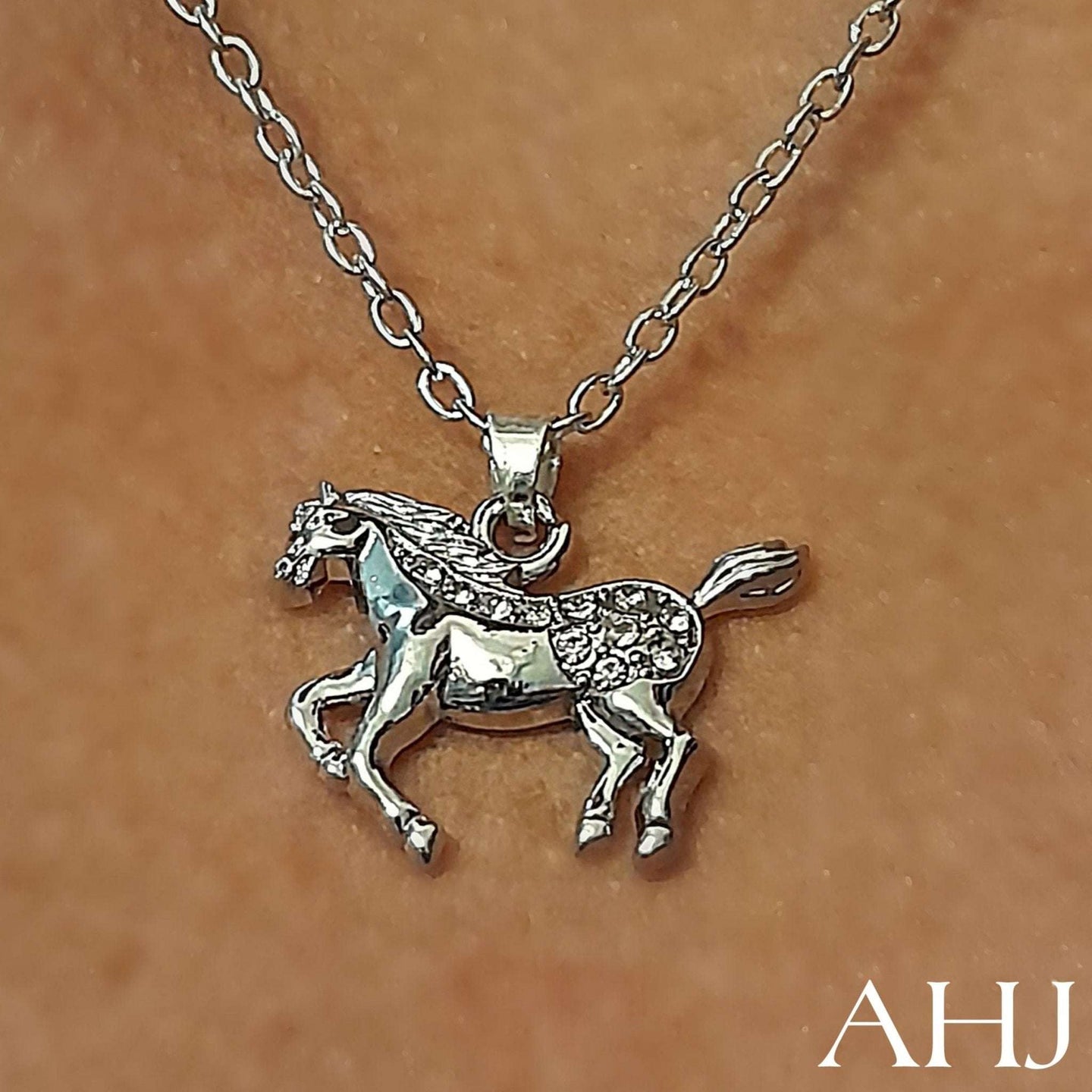 Spotted crystal silver horse pendant chain on person's neck.